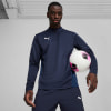 Ein Mann im dunkelblauen Trainingspullover hält einen Fußball.