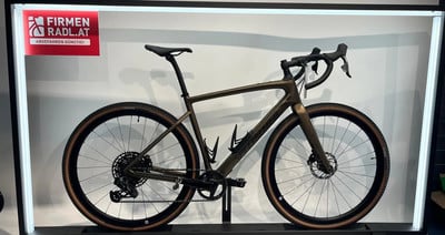 Ein braunes Gravelbike mit schwarzen Felgen und braunen Reifen steht auf einem Ständer. Ein braunes Gravelbike mit schwarzen Felgen und braunen Reifen steht auf einem Ständer.