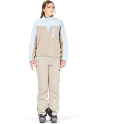 Eine Frau in einer beige Skihose und einer hellblau-beigen Jacke mit Kapuze.