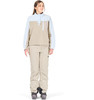 Eine Frau in einer beige Skihose und einer hellblau-beigen Jacke mit Kapuze.
