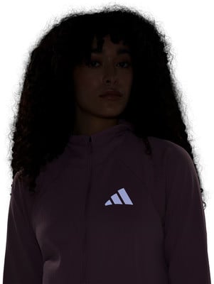 Eine Frau mit lockigem Haar trägt eine lila Jacke mit Adidas-Logo. Eine Frau mit lockigem Haar trägt eine lila Jacke mit Adidas-Logo.