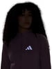 Eine Frau mit lockigem Haar trägt eine lila Jacke mit Adidas-Logo.