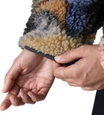 Eine Hand richtet den Saum einer flauschigen Jacke mit buntem Muster. Eine Hand richtet den Saum einer flauschigen Jacke mit buntem Muster.