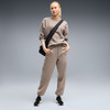Frau in beiger Jogginghose und Pullover mit schwarzer Umhängetasche.