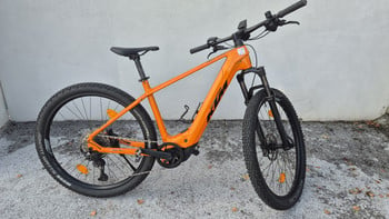 Ein orangefarbenes KTM E-Bike mit Federgabel und breiten Reifen steht an einer Wand.