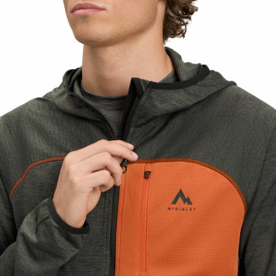 Mann schließt dunkle Kapuzenjacke mit orangefarbenem Einsatz und McKinley-Logo. Mann schließt dunkle Kapuzenjacke mit orangefarbenem Einsatz und McKinley-Logo.
