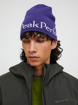 Ein junger Mann mit lockigem Haar trägt eine lila Mütze mit der Aufschrift Peak Performance.