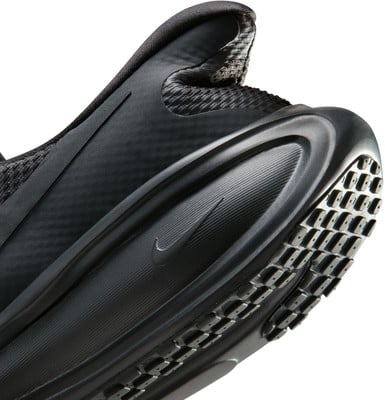 Detail černých bot Nike s výraznou podrážkou a logem.