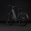 Graues Cube E-Bike mit Federung und Gepäckträger vor dunklem Hintergrund.