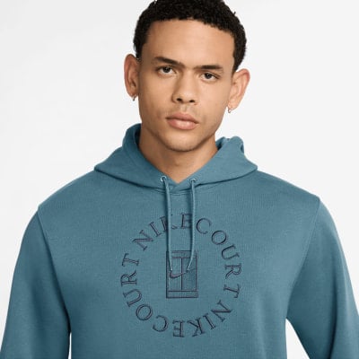 Ein Mann in einem blauen Kapuzenpullover mit Nike Court-Logo und einem Tennisplatz. Ein Mann in einem blauen Kapuzenpullover mit Nike Court-Logo und einem Tennisplatz.