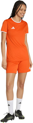 Frau im orangefarbenen Trikot und Shorts mit weißem Besatz, weißen Socken und Fußballschuhen.