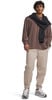 Ein Mann in einem braunen Langarmshirt mit schwarzem Pullover über den Schultern, beige Hose.