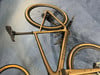 Ein goldenes Specialized Gravelbike mit beigen Reifen, das auf einer blauen Oberfläche liegt.
