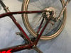 Detail eines dunkelroten Fahrradrahmens mit teilweise sichtbarem Hinterrad.