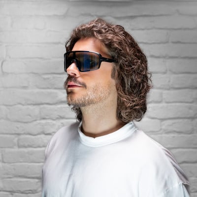 Mann mit lockigem Haar und Sonnenbrille vor weißer Ziegelwand. Mann mit lockigem Haar und Sonnenbrille vor weißer Ziegelwand.