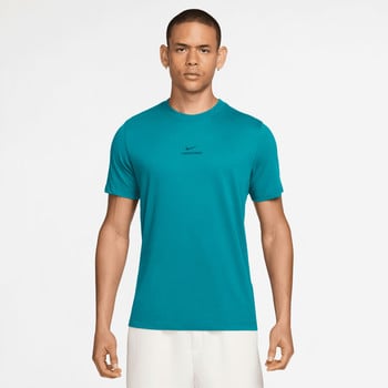 Ein Mann in einem türkisfarbenen Nike Pro T-Shirt und weißer Hose posiert vor weißem Hintergrund.