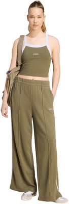 Eine Frau in einem grünen Top und weiten Adidas-Hosen mit einer Umhängetasche. Eine Frau in einem grünen Top und weiten Adidas-Hosen mit einer Umhängetasche.