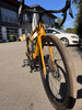 Gelbes Fahrrad auf einem Ständer vor einem Gebäude, weißes Auto im Hintergrund.