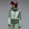 Eine Frau in einer hellgrünen Skijacke und Hose mit Helm.