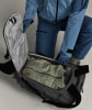 Person in blauer Skikleidung packt Jacke in Rucksack.