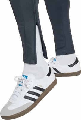 Nahaufnahme von Beinen in dunklen Hosen, weißen Socken und Adidas Samba Sneakers.