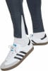 Nahaufnahme von Beinen in dunklen Hosen, weißen Socken und Adidas Samba Sneakers.