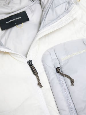 Detail einer Peak Performance Jacke mit weißen und grauen Teilen und Reißverschlüssen.