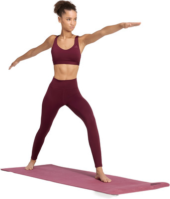 Eine Frau in weinroter Sportkleidung macht Yoga auf einer Matte. Eine Frau in weinroter Sportkleidung macht Yoga auf einer Matte.