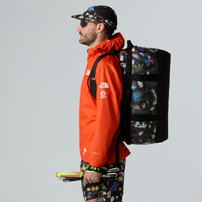 Ein Mann in einer orangefarbenen Jacke mit einer blumigen Tasche und Mütze hält Skistöcke. Ein Mann in einer orangefarbenen Jacke mit einer blumigen Tasche und Mütze hält Skistöcke.