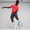 Ein Mann in einem pinken Shirt und blauen Shorts spielt mit einem Ball.
