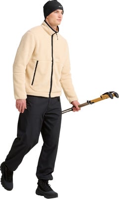 Ein Mann in einer cremefarbenen Fleecejacke und schwarzen Hosen hält Trekkingstöcke. Ein Mann in einer cremefarbenen Fleecejacke und schwarzen Hosen hält Trekkingstöcke.