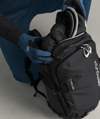 Eine Person packt einen Skihelm und Handschuhe in einen Rucksack. Eine Person packt einen Skihelm und Handschuhe in einen Rucksack.