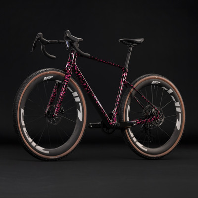 Ein pinkes Gravelbike mit schwarzen Details und braunen Felgen vor schwarzem Hintergrund. Ein pinkes Gravelbike mit schwarzen Details und braunen Felgen vor schwarzem Hintergrund.
