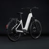 Ein weißes Cube E-Bike mit Gepäckträger und Schutzblechen vor dunklem Hintergrund.
