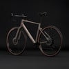 Ein braunes Cube Gravelbike mit schwarzen Felgen und braunen Reifen vor dunklem Hintergrund.