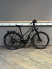 Ein schwarzes KTM E-Bike steht auf einem Holzboden vor einer grauen Wand.
