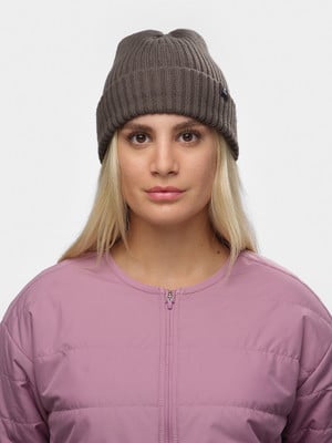 Junge Frau mit blonden Haaren trägt eine braune Mütze und eine rosa Jacke.