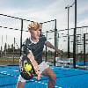 Ein junger Mann spielt Padel auf einem blauen Platz mit einem Schläger in der Hand.