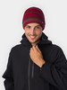 Ein Mann in einer gestrickten Mütze und schwarzer Jacke lächelt.