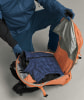 Eine Person in blauer Kleidung packt eine Daunenjacke in einen orangefarbenen Rucksack.