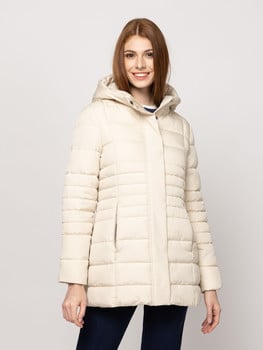 Egy nő krémszínű, kapucnis pufidzsekiben és sötét farmerben mosolyog.