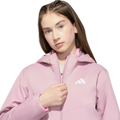 Mädchen in einer rosa Jacke mit Adidas-Logo auf weißem Hintergrund. Mädchen in einer rosa Jacke mit Adidas-Logo auf weißem Hintergrund.