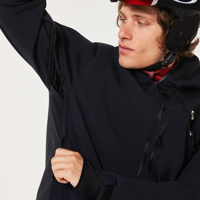Mann in schwarzer Skijacke mit hochgezogener Kapuze und Hand unter dem Arm.