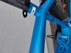 Blauer Fahrradrahmen mit schwarzen Details und weißem Etikett.