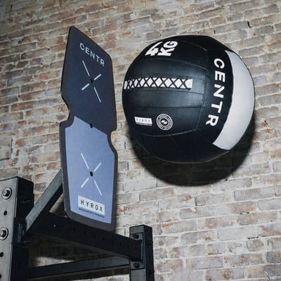 Ein schwarzer Medizinball mit weißem Streifen hängt an der Wand neben einer Zielscheibe.