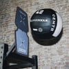 Ein schwarzer Medizinball mit weißem Streifen hängt an der Wand neben einer Zielscheibe.