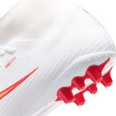 Detail eines weißen Nike-Fußballschuhs mit roten Stollen und goldenem Logo. Detail eines weißen Nike-Fußballschuhs mit roten Stollen und goldenem Logo.
