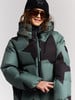 Mädchen in grüner Daunenjacke mit schwarzen Sternen und schwarzer Mütze.