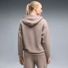 Frau in brauner Kapuzenjacke und Jogginghose, Rückansicht.