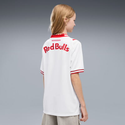 Mädchen in einem weißen Red Bulls Trikot mit roten Details vor grauem Hintergrund.
